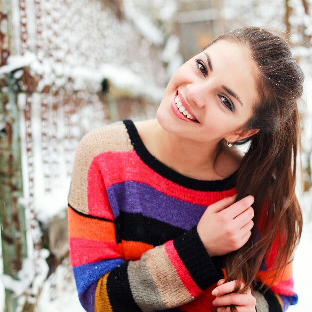 Chica sonriente con cola de caballo y suéter colorido en un día de nieve