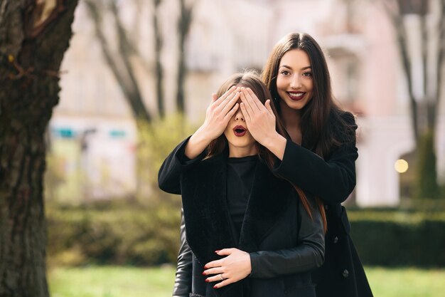 Chica sonriente cubriendo los ojos a su amiga