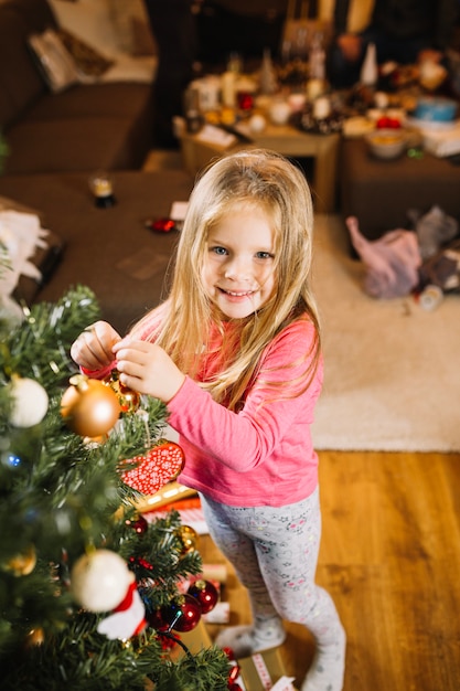 Chica sonriente decorando árbol de navidad