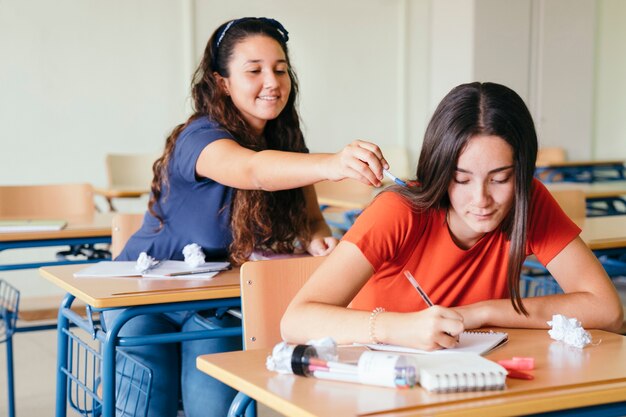 Chica sonriente distrayendo a su compañera de clase