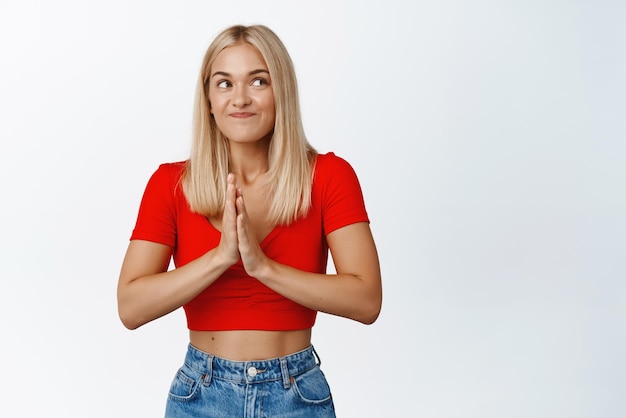 Chica sonriente esperanzada esperando con emoción frotarse las manos y esperar a disfrutar esperando buenas noticias de pie en traje de verano contra el fondo blanco.