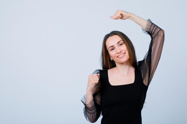 Chica sonriente está bailando levantando su puño sobre fondo blanco.