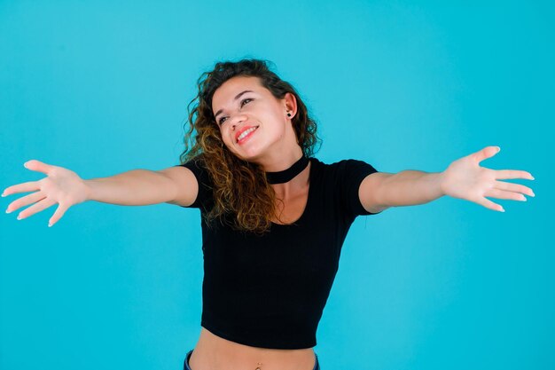 Chica sonriente está mirando hacia arriba abriendo sus manos sobre fondo azul.