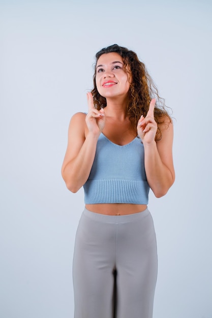 Chica sonriente está mirando hacia arriba señalando con el dedo índice sobre fondo blanco.