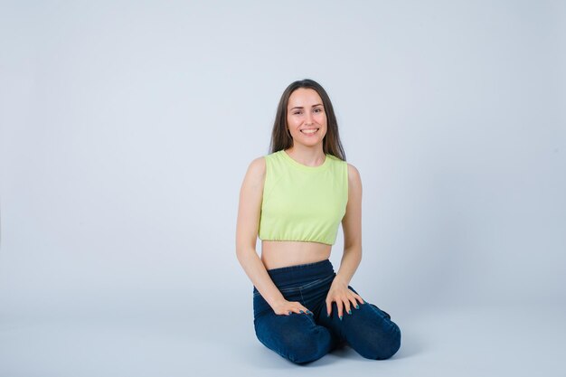 Chica sonriente está mirando a la cámara sentada en el suelo sobre fondo blanco.