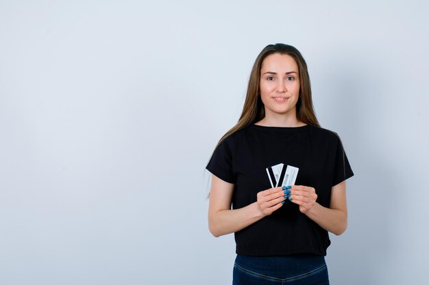 Chica sonriente está mirando a la cámara sosteniendo tarjetas de crédito sobre fondo blanco.