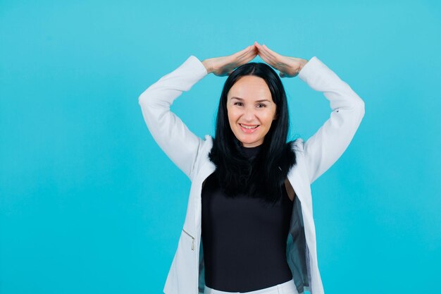 Chica sonriente está sosteniendo ahnds por encima de la cabeza sobre fondo azul.