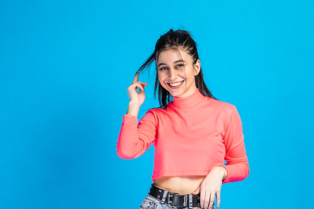 Chica sonriente de fondo azul y estirando su cabello Foto de alta calidad