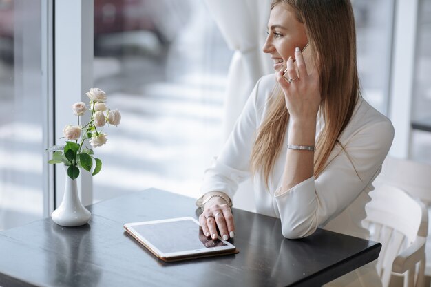 Chica sonriente hablando por teléfono con una tablet sobre la mesa