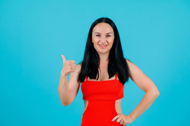 La chica sonriente muestra un gesto perfecto y se pone la otra mano en la cintura con fondo azul.