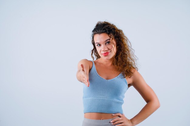 La chica sonriente muestra un gesto de saludo extendiendo la mano a la cámara con fondo blanco