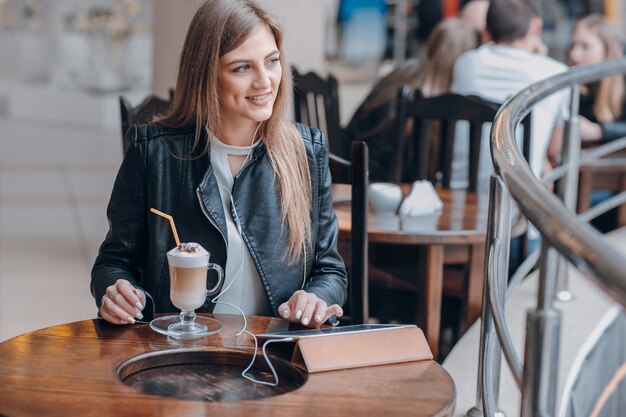 Chica sonriente con una tablet y un batido en una mesa