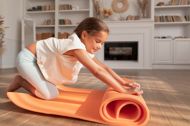 Chica sonriente de tiro completo con estera de yoga