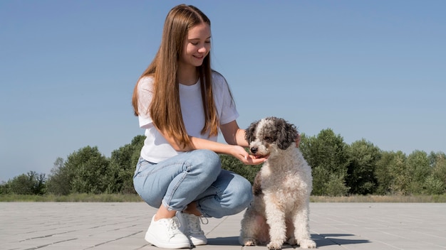 Chica sonriente de tiro completo con perro al aire libre