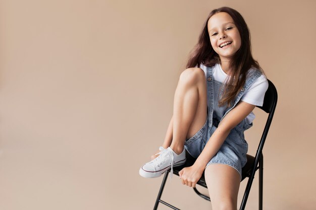 Chica sonriente de tiro medio sentada en una silla