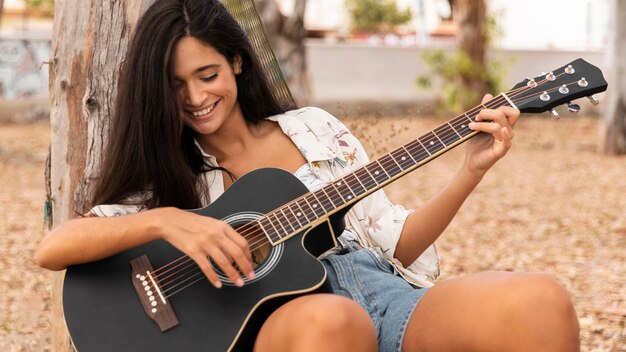 Chica sonriente de tiro medio tocando la guitarra