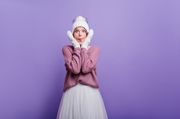 Chica sorprendida divertida en traje de invierno tocando su rostro. maravillosa mujer blanca en ropa de lana que expresa asombro.