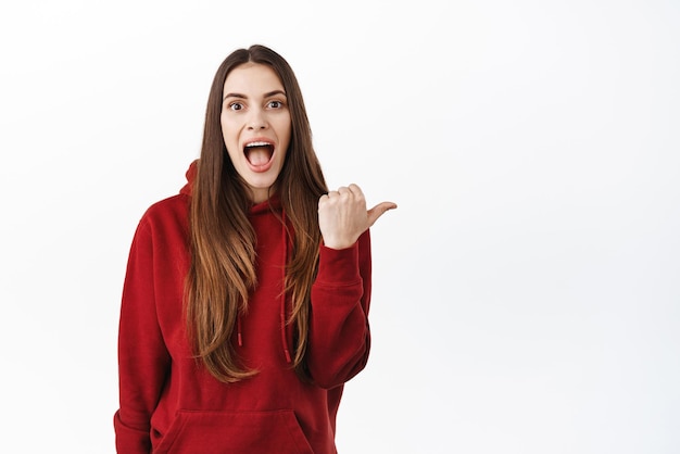 Foto gratuita chica sorprendida y emocionada mirando la mejor oferta promocional increíble en la tienda señalando a un lado el espacio de copia correcto y la mandíbula caída fascinada mirando el fondo blanco impresionado de la cámara