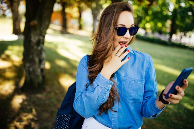 Chica sorprendida escuchando música en línea y viendo contenido multimedia al aire libre en un parque