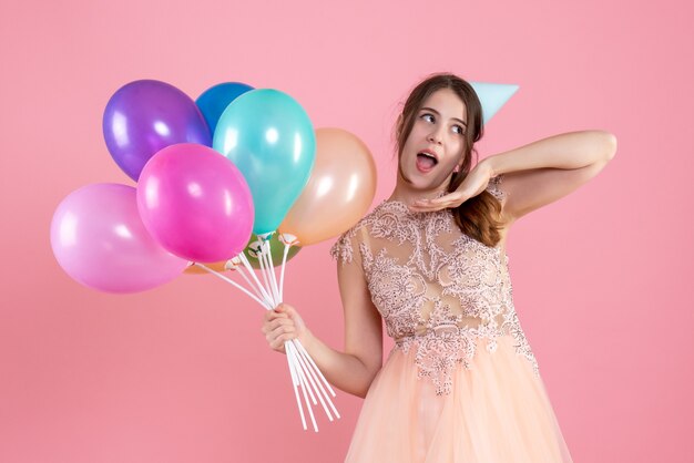 Chica sorprendida con gorro de fiesta sosteniendo globos en rosa