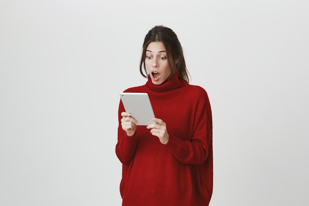 Chica sorprendida mirando la pantalla de la tableta digital sorprendida