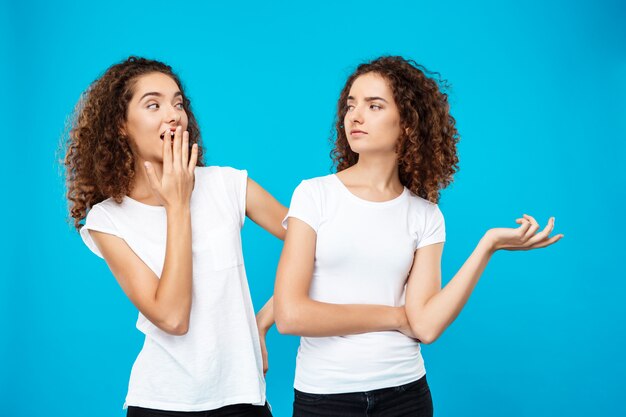 Chica sorprendida mirando a su hermana gemela sobre pared azul