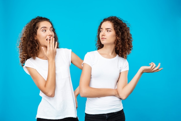 Chica sorprendida mirando a su hermana gemela sobre pared azul