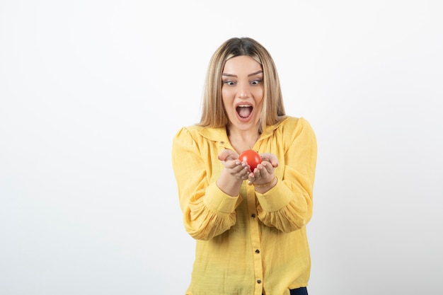 chica sorprendida mirando tomate rojo sobre blanco.