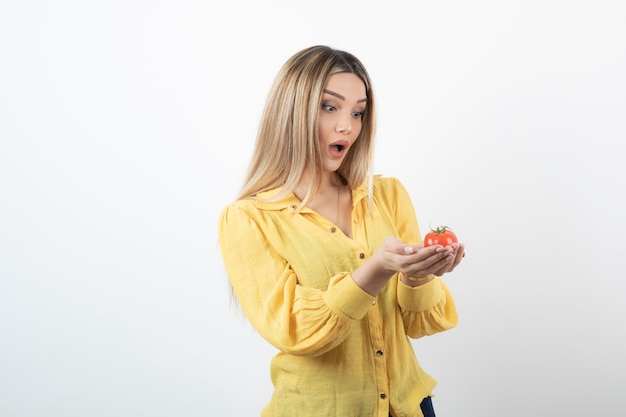 chica sorprendida mirando tomate rojo sobre blanco.