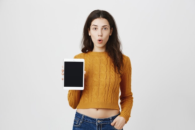 Chica sorprendida mostrando promo de aplicación, pantalla de tableta digital