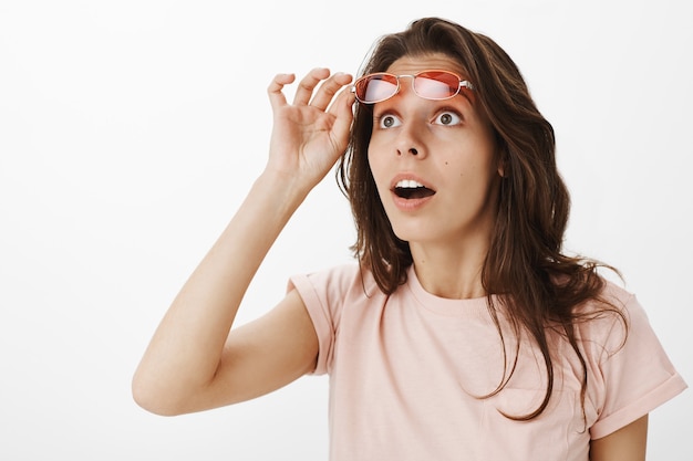 Foto gratuita chica sorprendida y sorprendida con gafas de sol posando contra la pared blanca