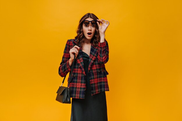 Chica sorprendida en vestido negro mirando al frente en la pared aislada