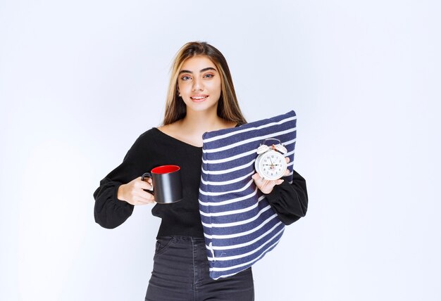 Chica sosteniendo una almohada azul y una taza de café por la mañana.