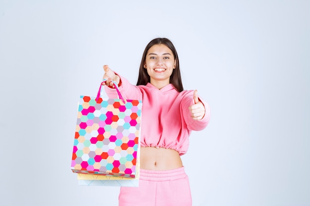 Chica sosteniendo bolsas de colores y parece emocionada.