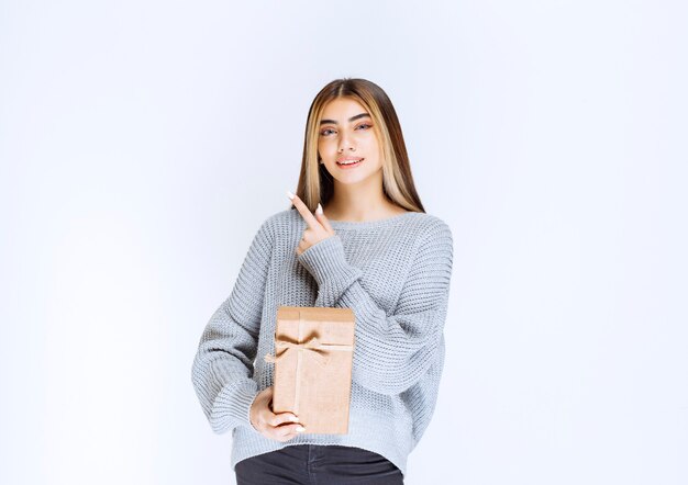 Chica sosteniendo una caja de regalo de cartón y apuntando un receptor a un lado.