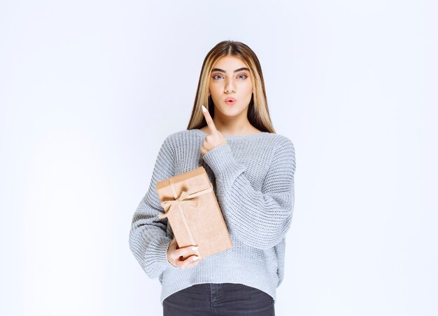 Chica sosteniendo una caja de regalo de cartón y apuntando un receptor a un lado.