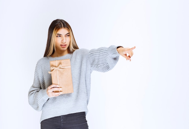 Chica sosteniendo una caja de regalo de cartón y apuntando un receptor a un lado.