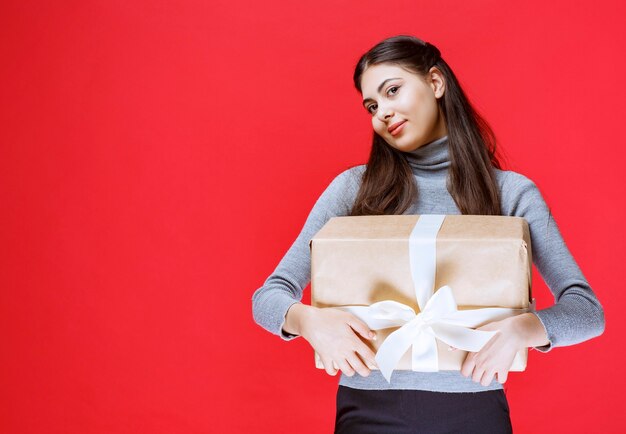 Chica sosteniendo una caja de regalo de cartón envuelta con cinta de tul blanco.