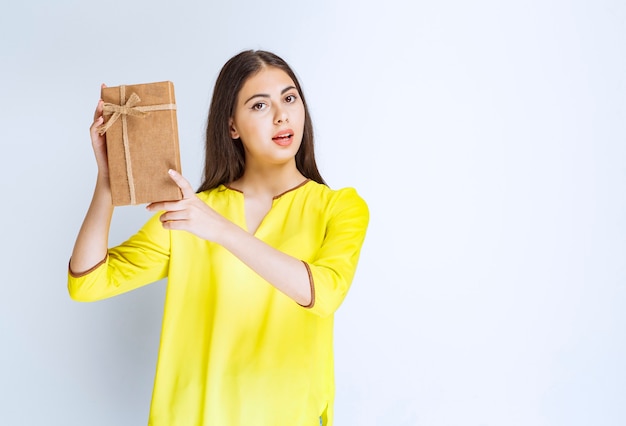 Chica sosteniendo una caja de regalo de cartón y parece confiada o pensativa.