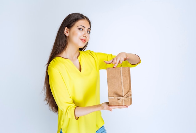 Chica sosteniendo una caja de regalo de cartón y sintiéndose positiva.