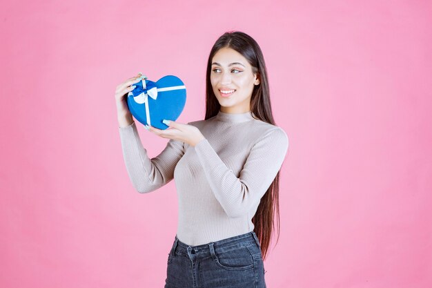 Chica sosteniendo una caja de regalo en forma de corazón azul y demostrándolo