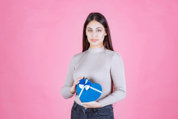 Chica sosteniendo una caja de regalo en forma de corazón azul y demostrándolo