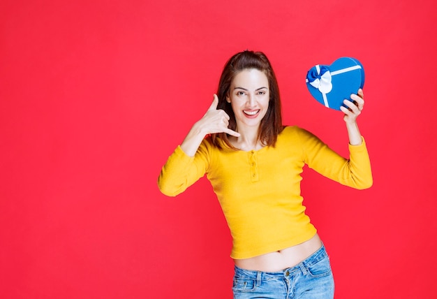 Chica sosteniendo una caja de regalo con forma de corazón azul y pidiendo una llamada
