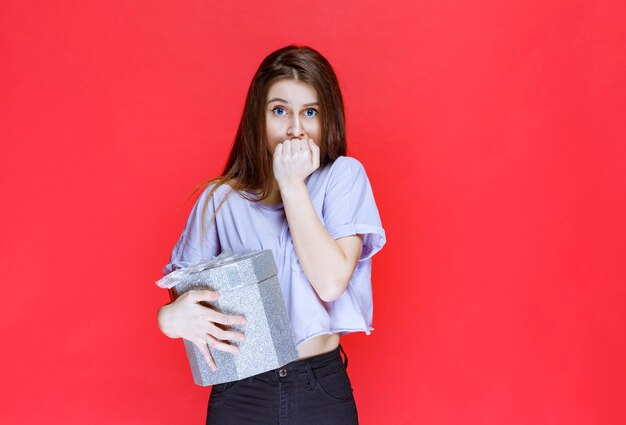 Chica sosteniendo una caja de regalo plateada y parece deprimida y confundida.