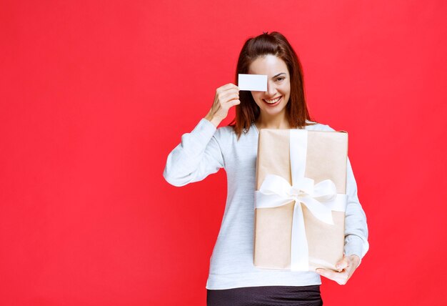 Chica sosteniendo una caja de regalo y presentando su tarjeta de visita.