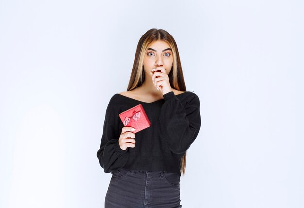 Chica sosteniendo una caja de regalo roja y parece aterrorizada. Foto de alta calidad