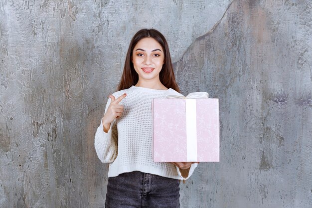 Chica sosteniendo una caja de regalo violeta envuelta con cinta blanca.