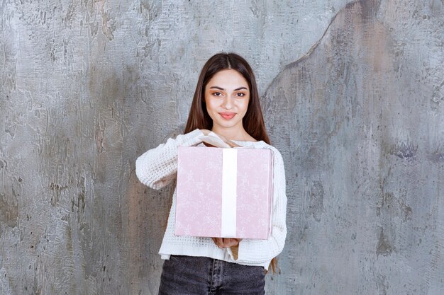 Chica sosteniendo una caja de regalo violeta envuelta con cinta blanca.