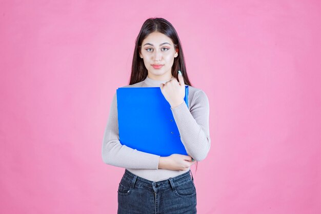 Chica sosteniendo una carpeta de informe azul y parece cansada