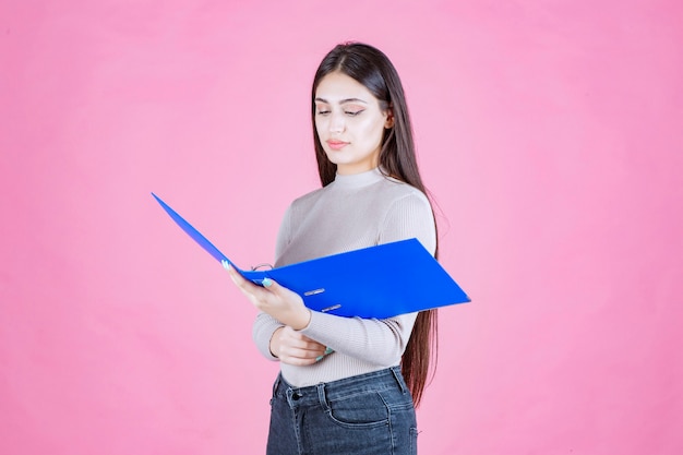 Chica sosteniendo una carpeta de informe azul y parece cansada